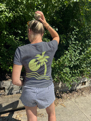 Woman in grey shirt with yellow art deco type image of a palm tree and sun over water
