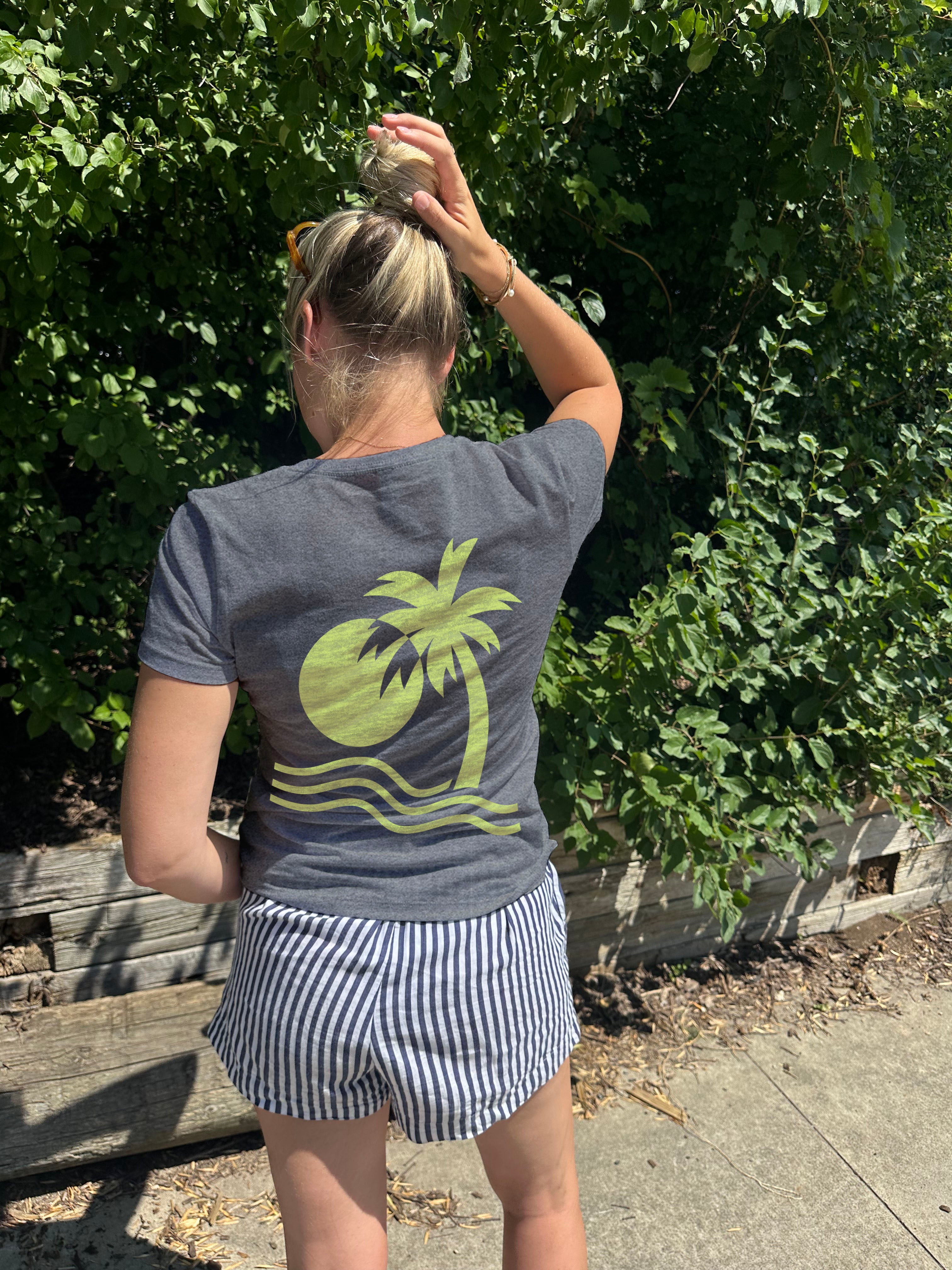Woman in grey shirt with yellow art deco type image of a palm tree and sun over water